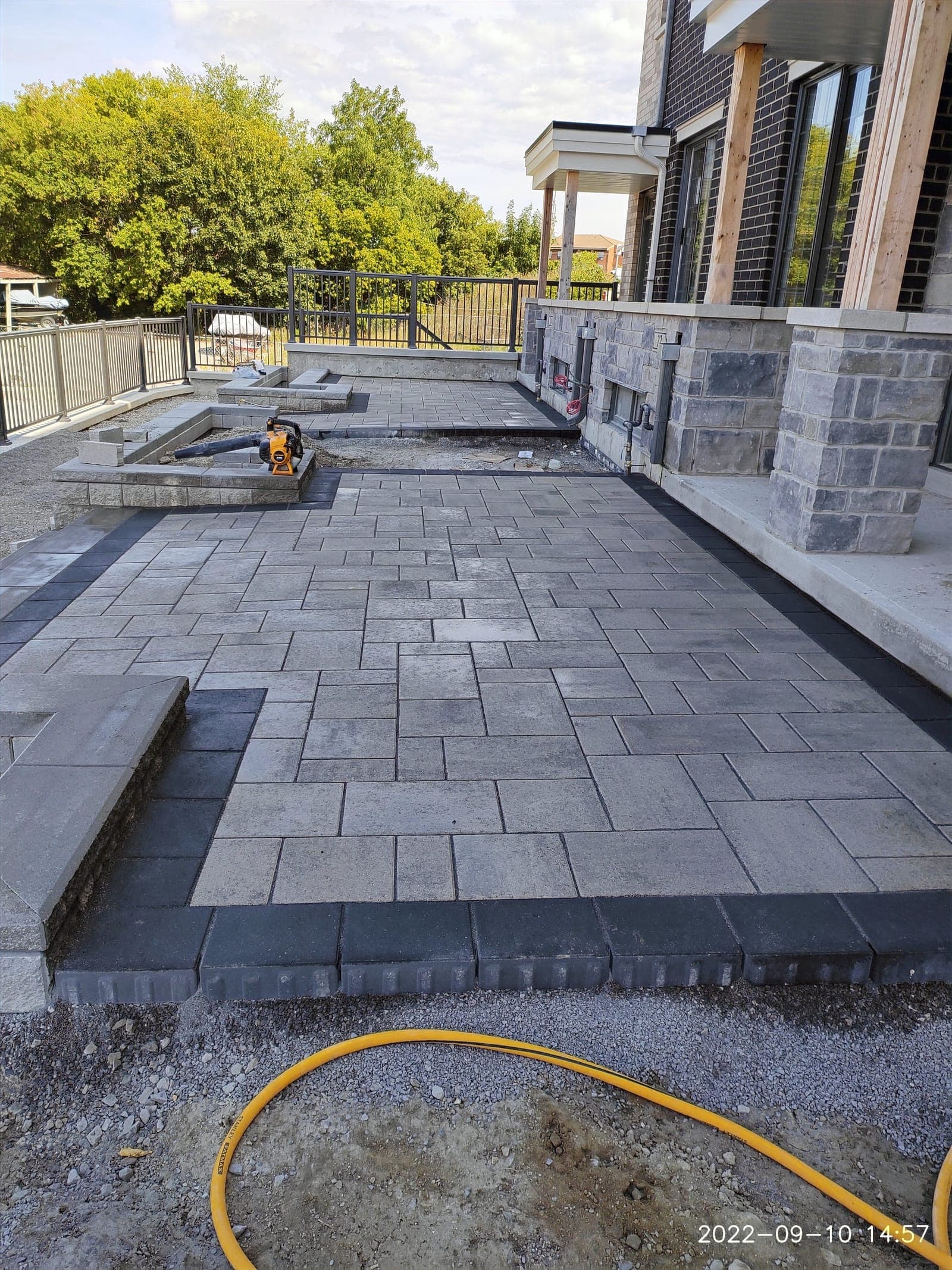 Maxinity crew finishing an interlock patio behind a stone home